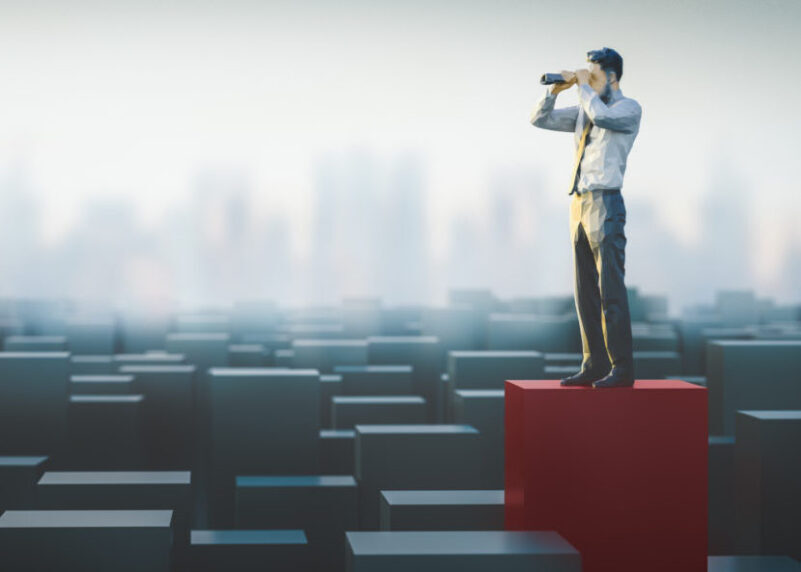 Un hombre de pie sobre una caja roja, observando a través de unos binoculares.